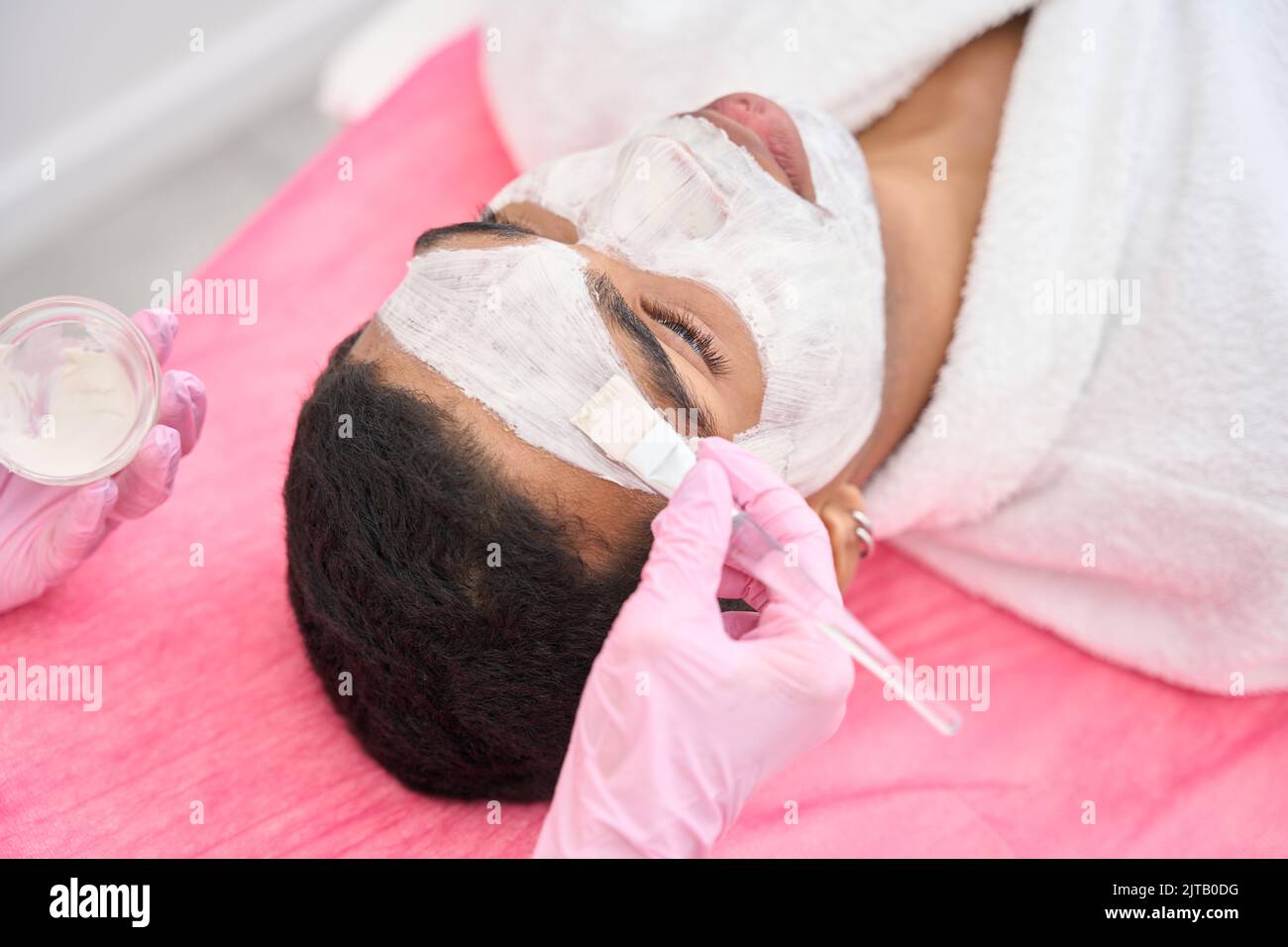 Estetista applicare maschera a faccia di cliente maschile con pennello Foto Stock