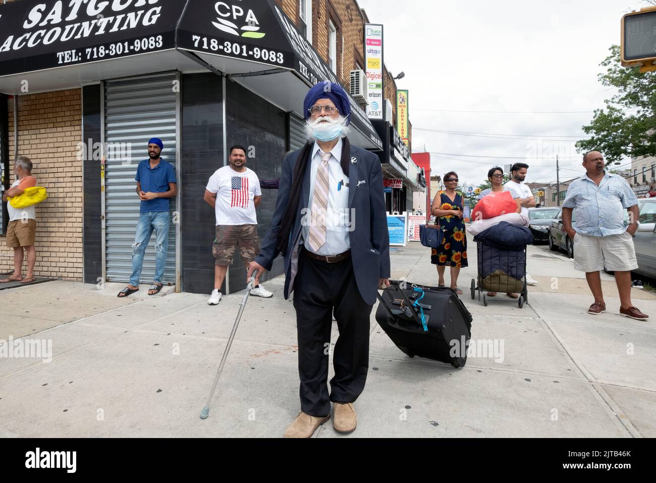 Una scena stradale sulla 101st Avenue con un viaggiatore Sikh in primo piano e altri uomini e donne che camminano e si appendono fuori. Nel Queens, New York. Foto Stock