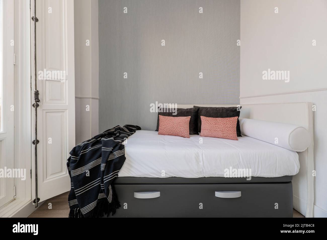 Camera da letto con testata imbottita in tessuto bianco, cuscini e cuscini coordinati, pavimento in legno di castagno, graziosi dettagli con cuscini rosa e coordinati Foto Stock
