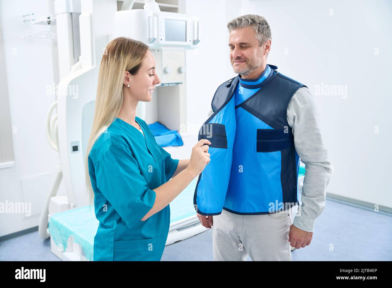 Il medico biondo lancia un abito protettivo blu sul paziente Foto Stock