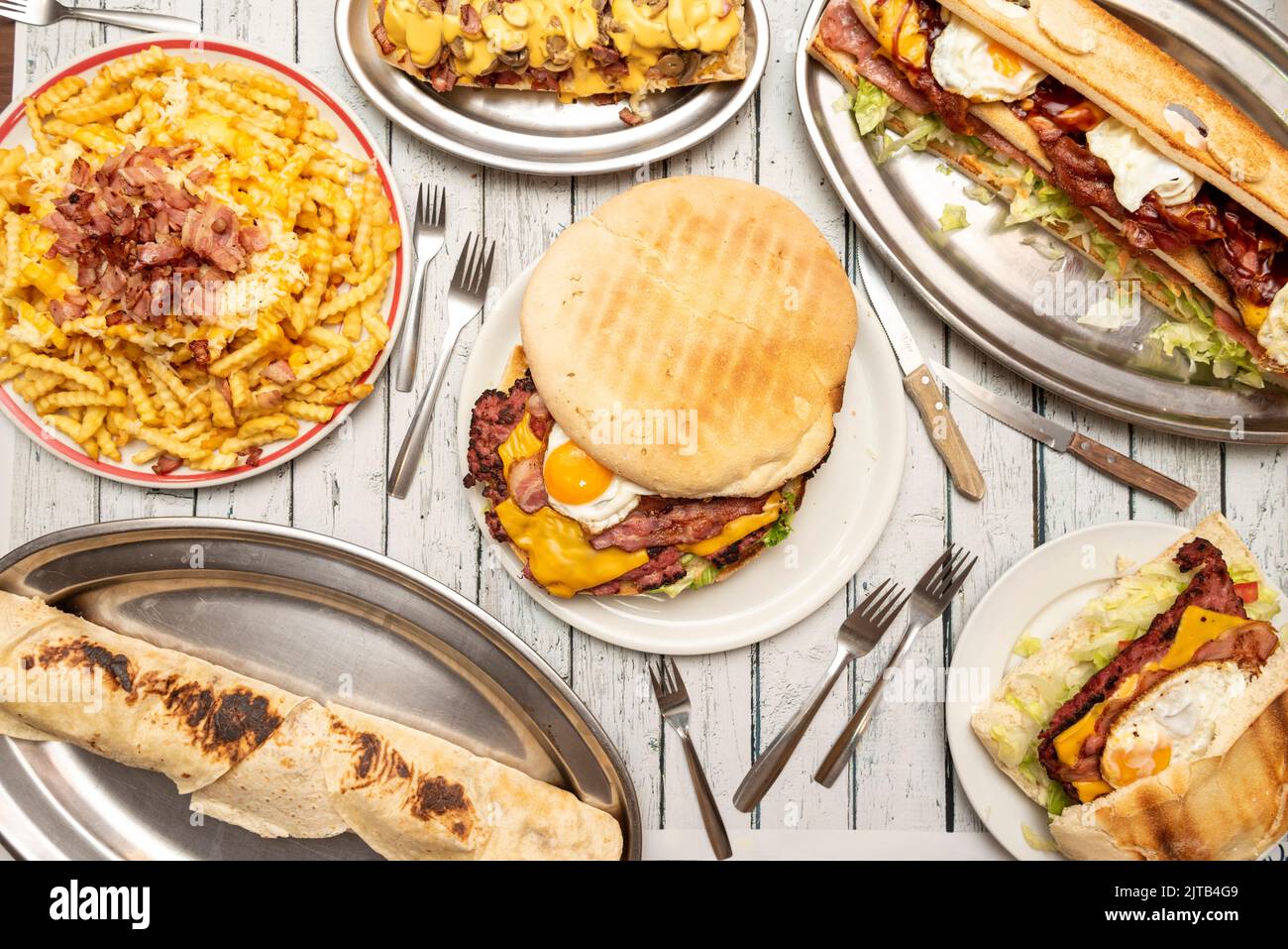 Set di piatti con cibi selvaggi, hamburger grande con uova, pancetta fritta e formaggio fuso, sandwich con gli stessi ingredienti, patatine fritte con formaggio e pancetta Foto Stock
