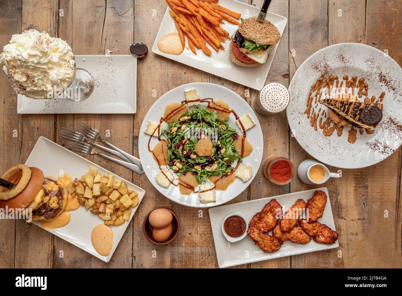 Set di fast food con insalate e pezzo di torta, hamburger con patatine fritte, insalata con formaggio e cotogna, pollo più piccante Foto Stock