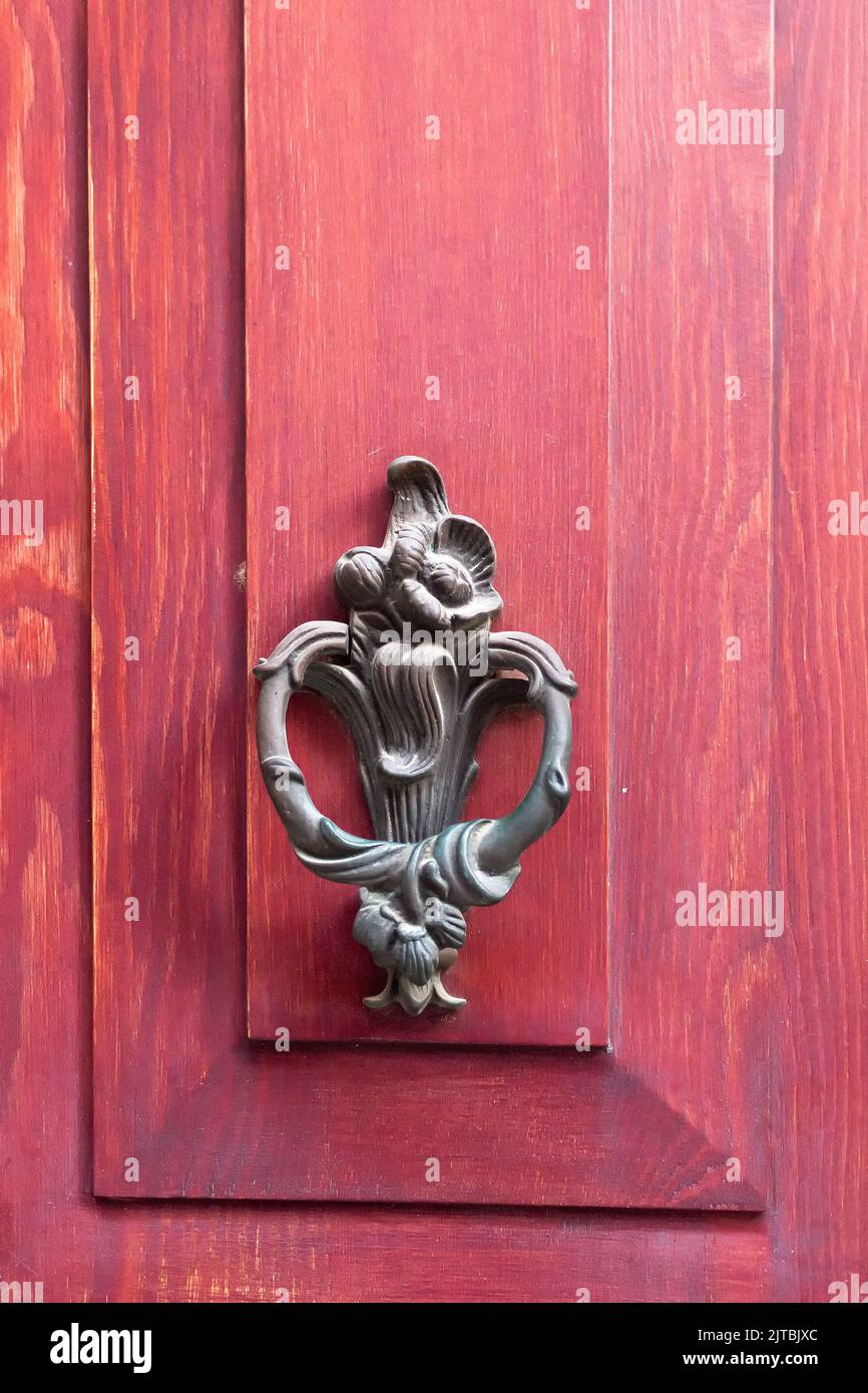 Vista ravvicinata del vecchio, tradizionale, pomello della porta ornamentale su sfondo di legno rosso. Foto Stock