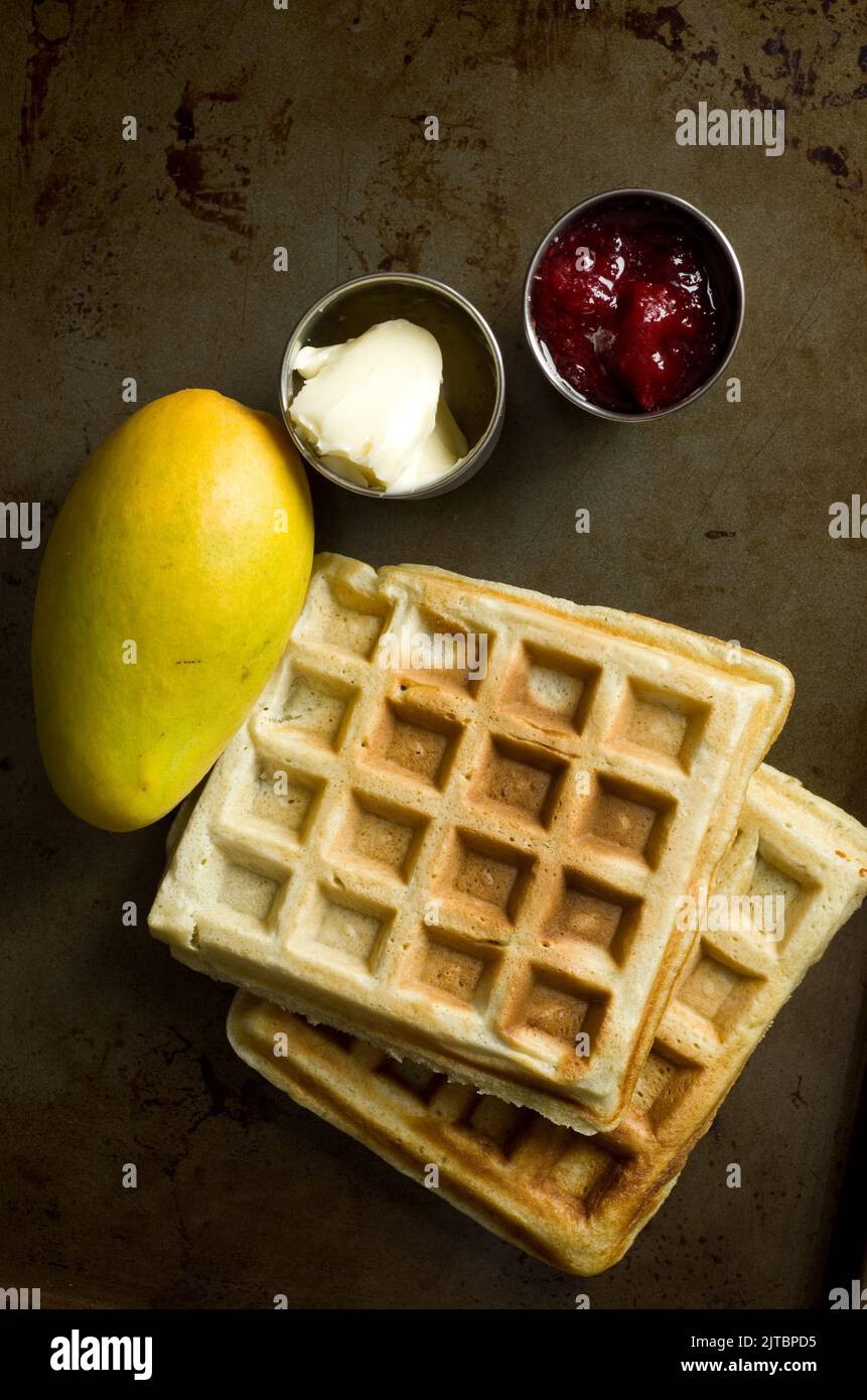 Deliziosi waffle fatti in casa con confettura di fragole, burro e mango verticale Foto Stock