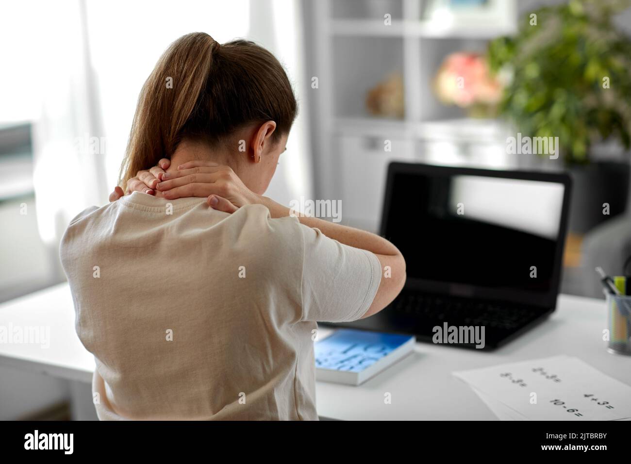 insegnante stanco con un notebook che tocca il collo a casa Foto Stock