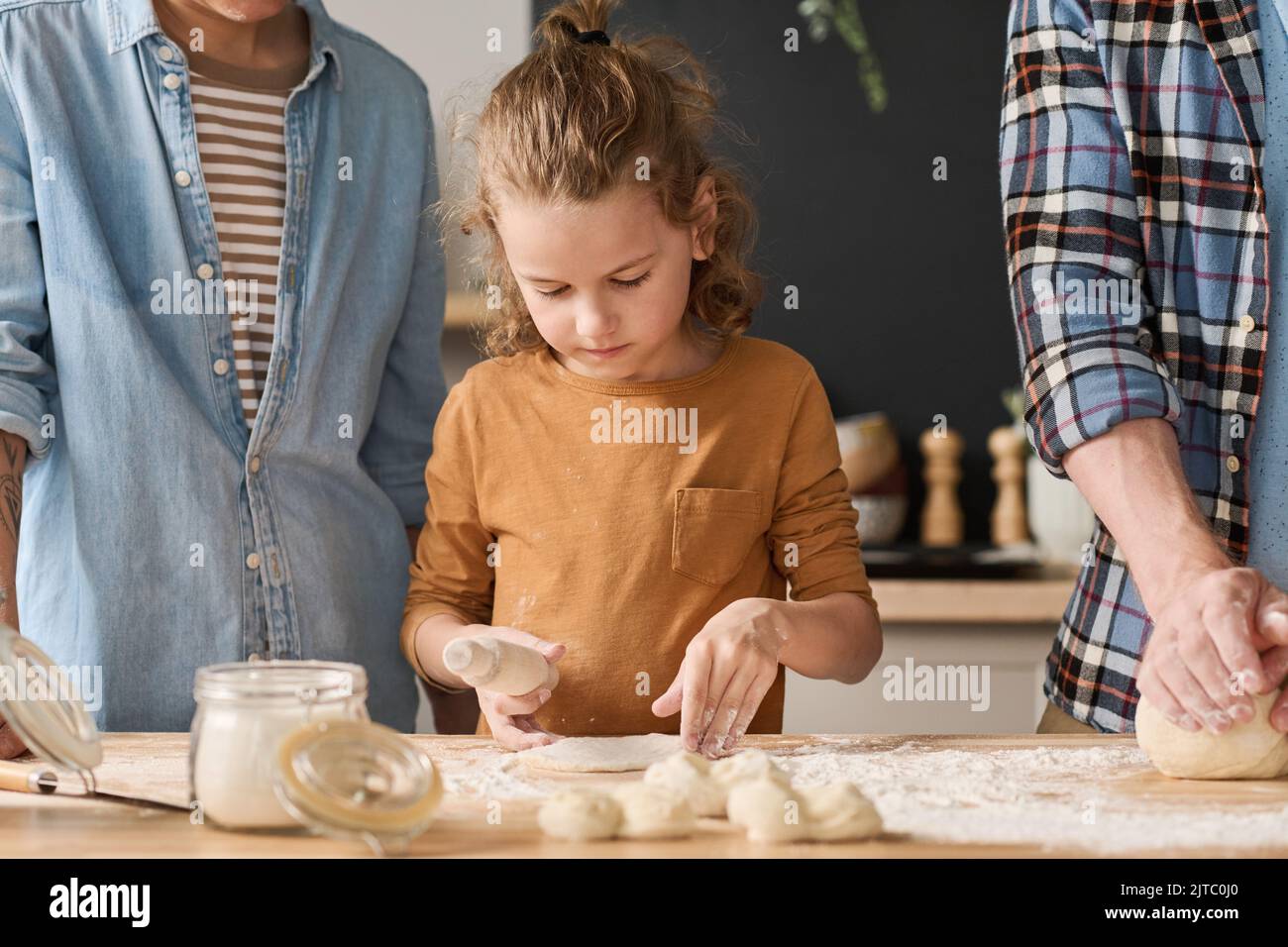 Bambino imparando a cuocere la torta da impasto insieme ai suoi genitori a tavola Foto Stock