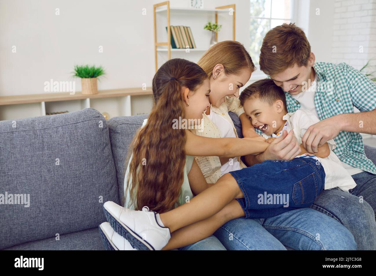 Famiglia allegra con bambini che si divertono insieme e che si divertono a fare il solletico sul divano del soggiorno Foto Stock