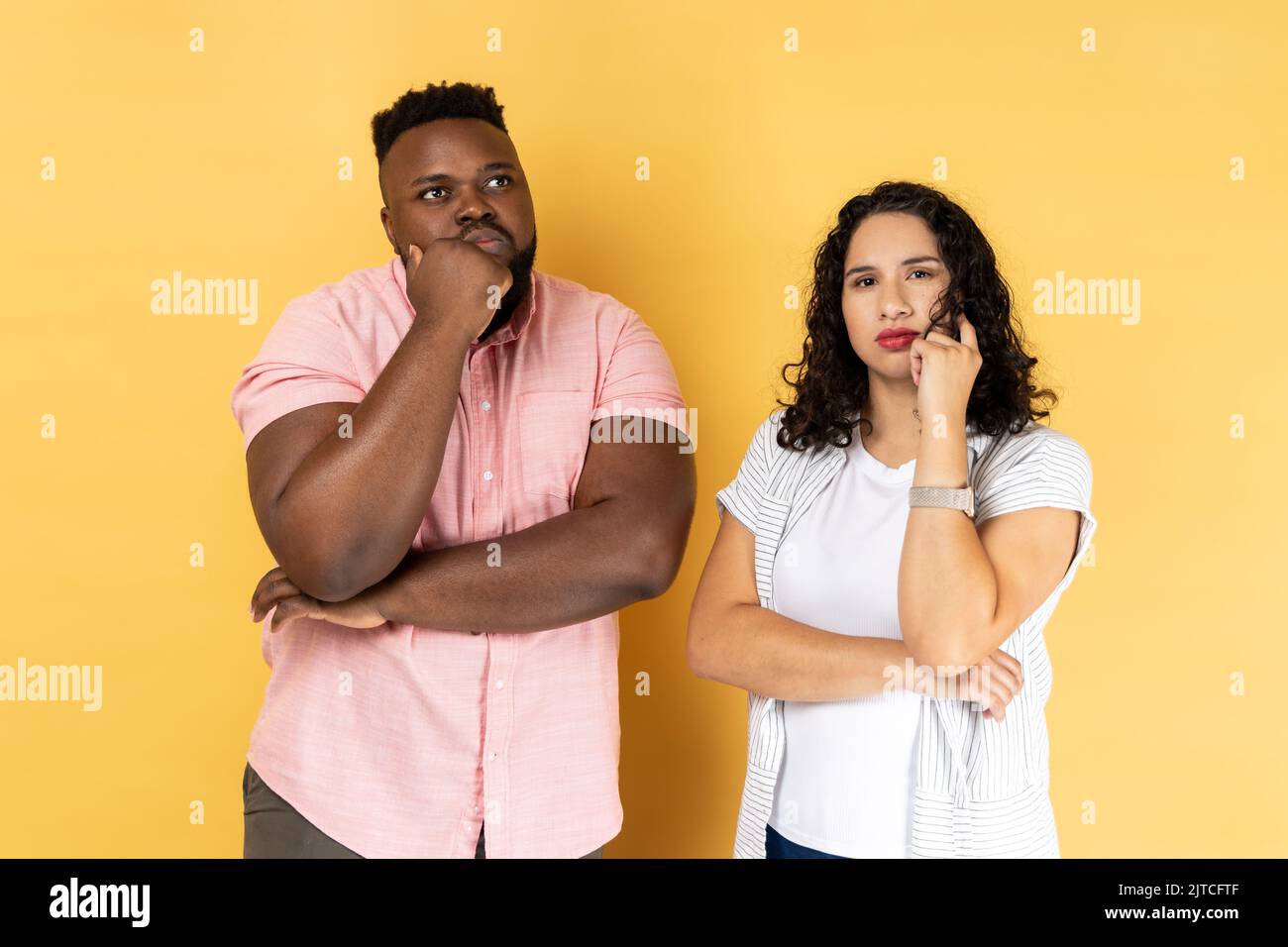 Ritratto di giovane coppia premurosa in abbigliamento casual in piedi insieme, tenendo i loro chins mentre pensando soluzione, guardando lontano. Studio al coperto isolato su sfondo giallo. Foto Stock