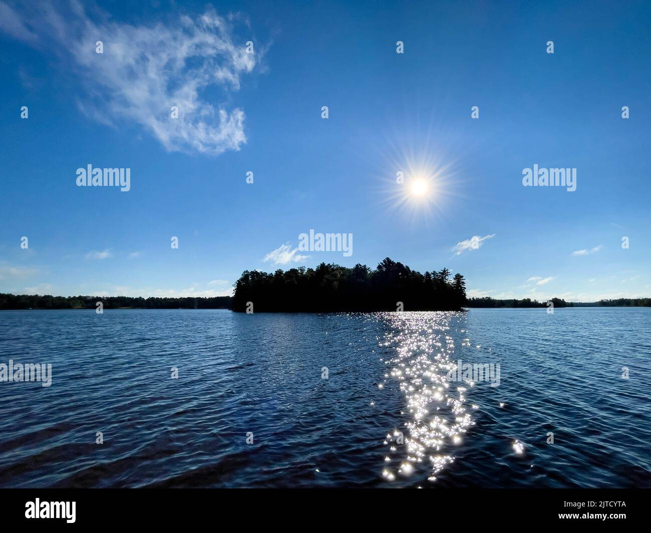 Lago con un'isola e il sole che splana sull'acqua, orizzontale Foto Stock