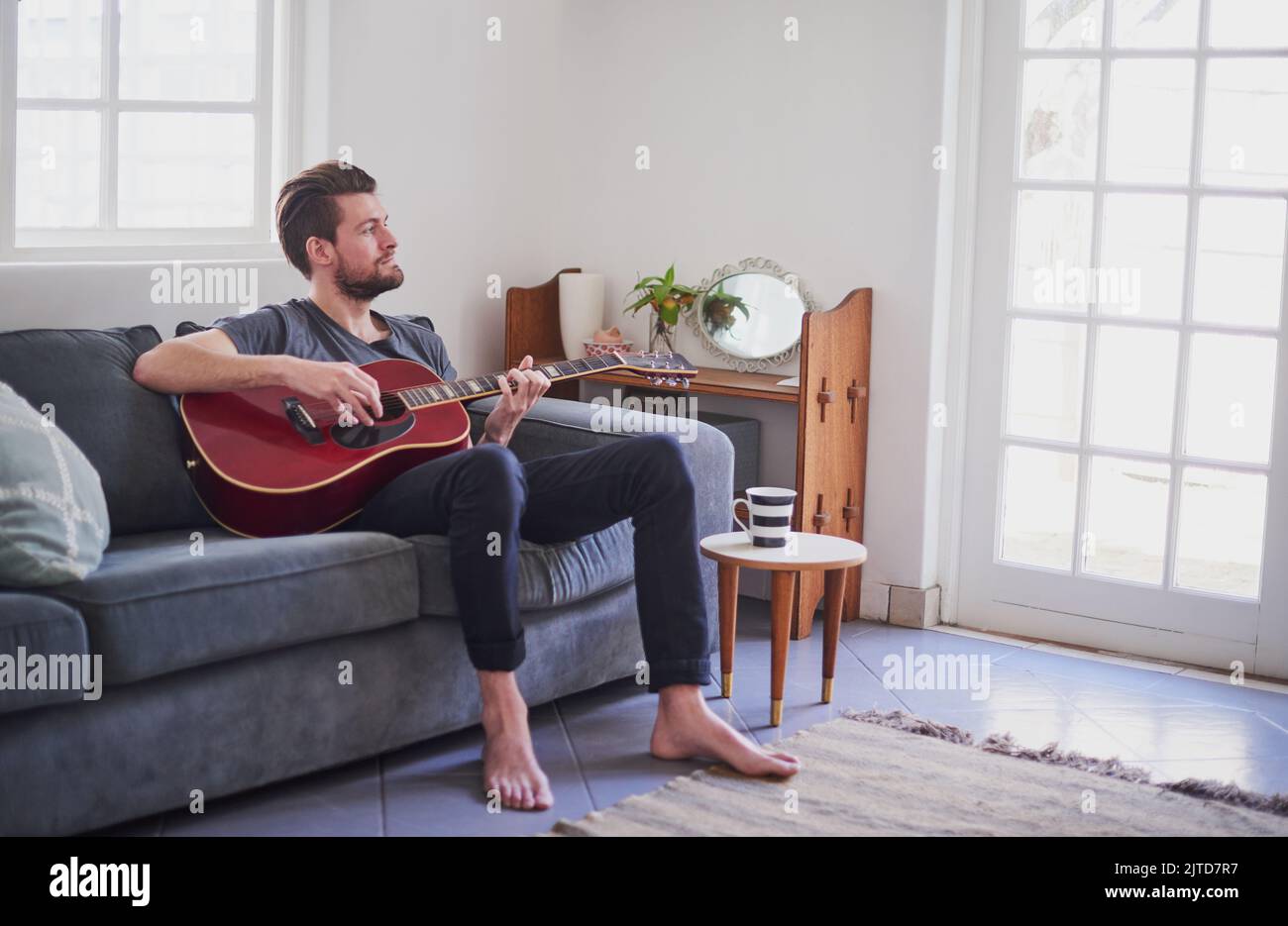 La chitarra impiega del tempo per padroneggiare, un bel giovane che suona una chitarra a casa. Foto Stock