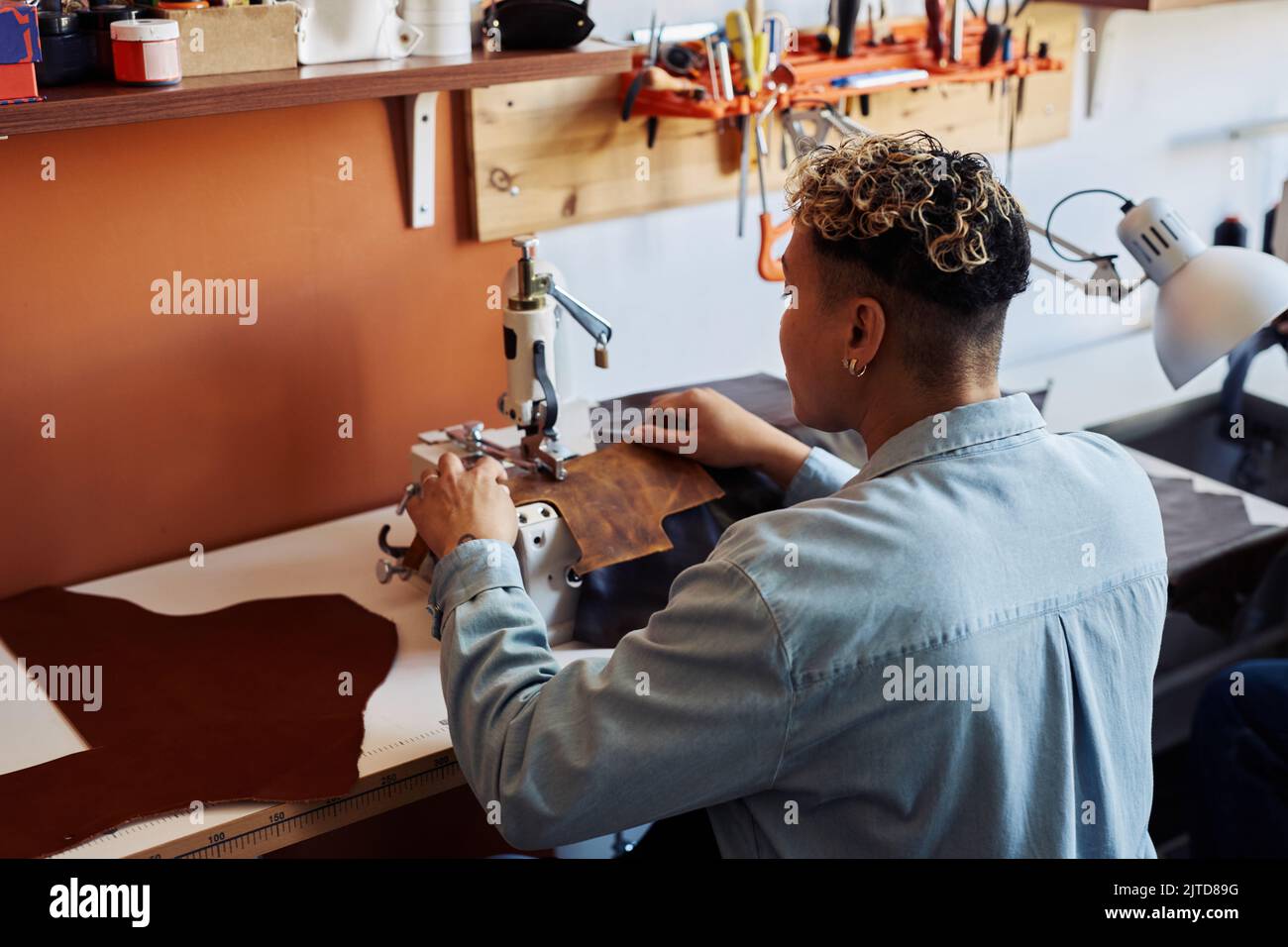 Vista posteriore dell'artigiano che utilizza la macchina da cucire nel negozio di pelletteria, spazio copia Foto Stock