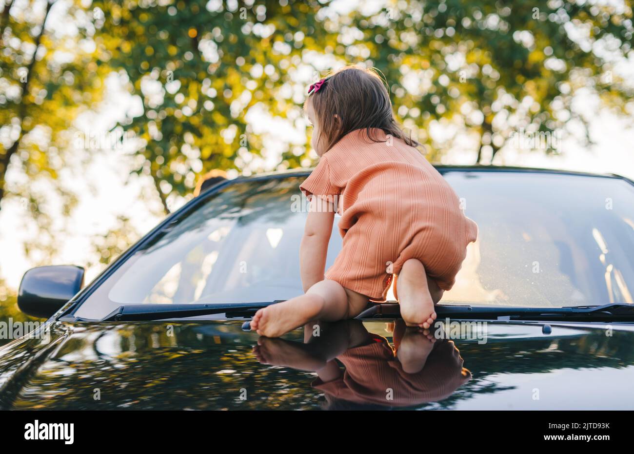 Il bambino che striscio a quattro zampe sul cappuccio dell'auto di suo padre. Bambini attivi che giocano all'aperto. Famiglia felice, infanzia. Foto Stock