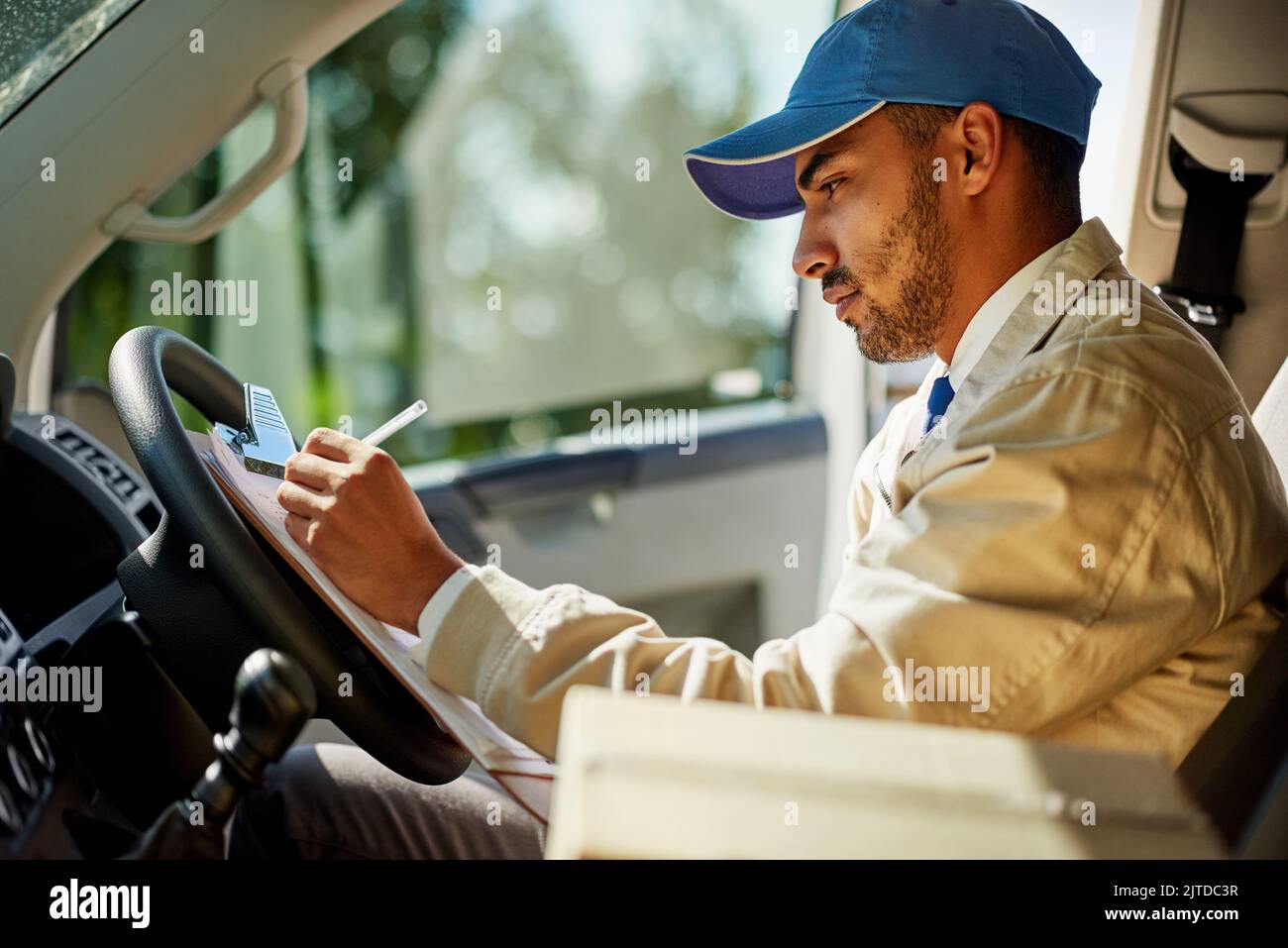 Mantenere i tempi di consegna richiede un po' di concentrazione: Un addetto alla consegna che scrive su un clipboard mentre si siede nel suo furgone. Foto Stock