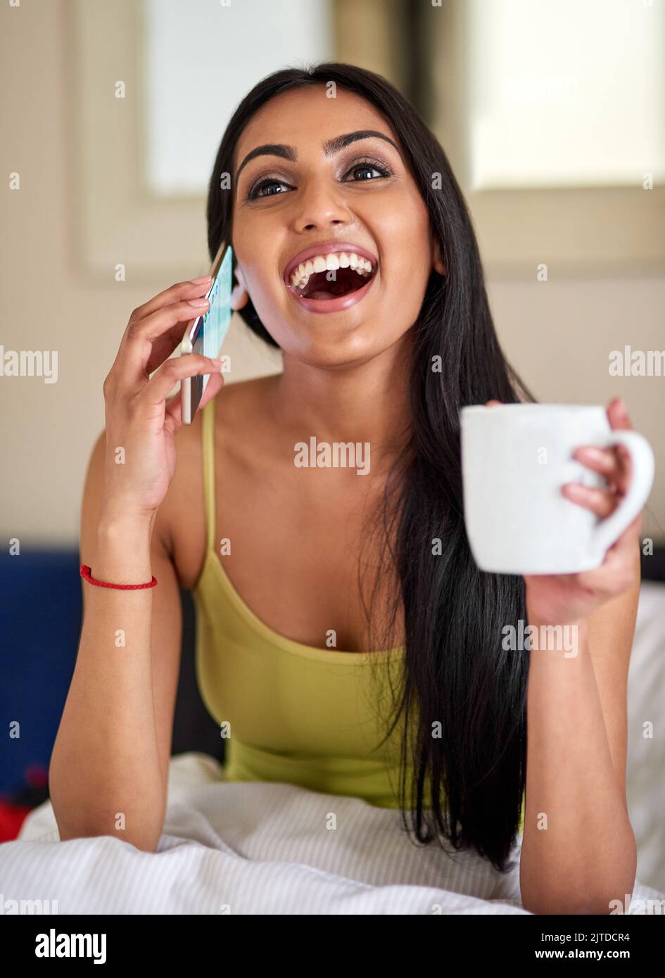 Mattina motivazione da una buona chiamata di notizie. Una giovane donna felice che parla al telefono nel letto. Foto Stock