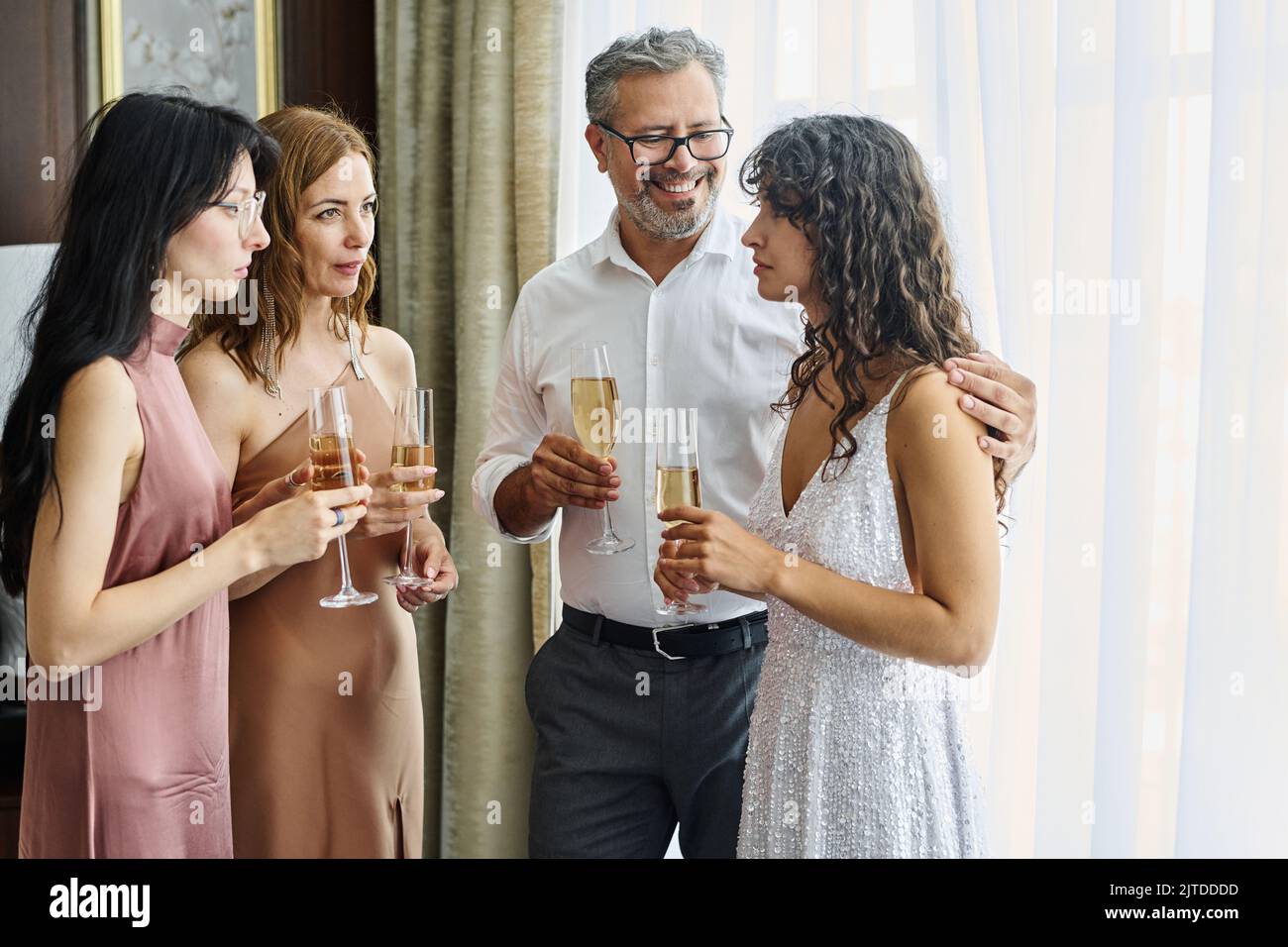 Felice uomo maturo con flauto di champagne che abbraccia la sua bella figlia in abito da sposa mentre si gode la festa con la famiglia Foto Stock