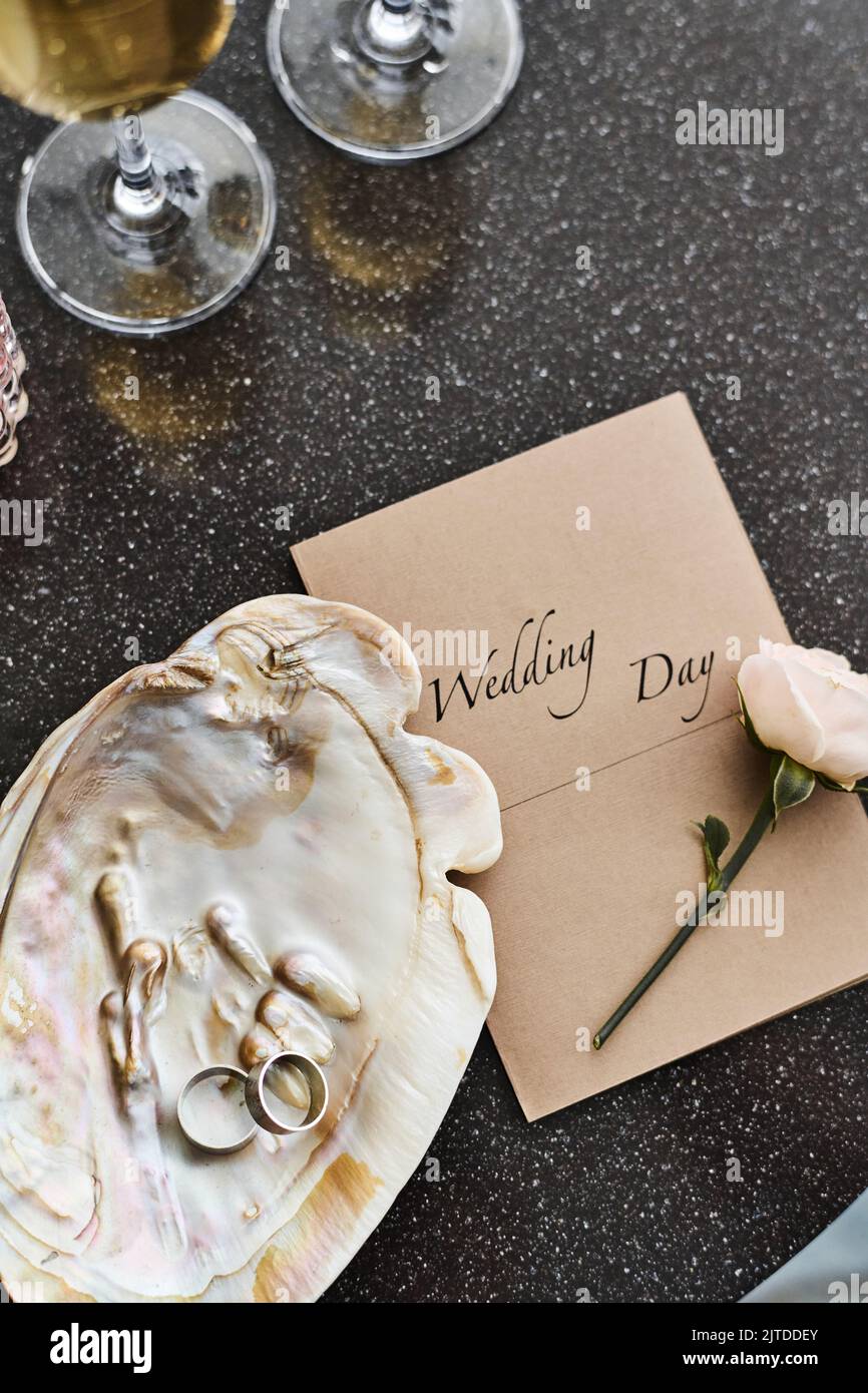 Flatlay di matrimonio composizione di conchiglia in perla con due anelli, invito, rosa bianca fresca e flauti con champagne sul tavolo Foto Stock