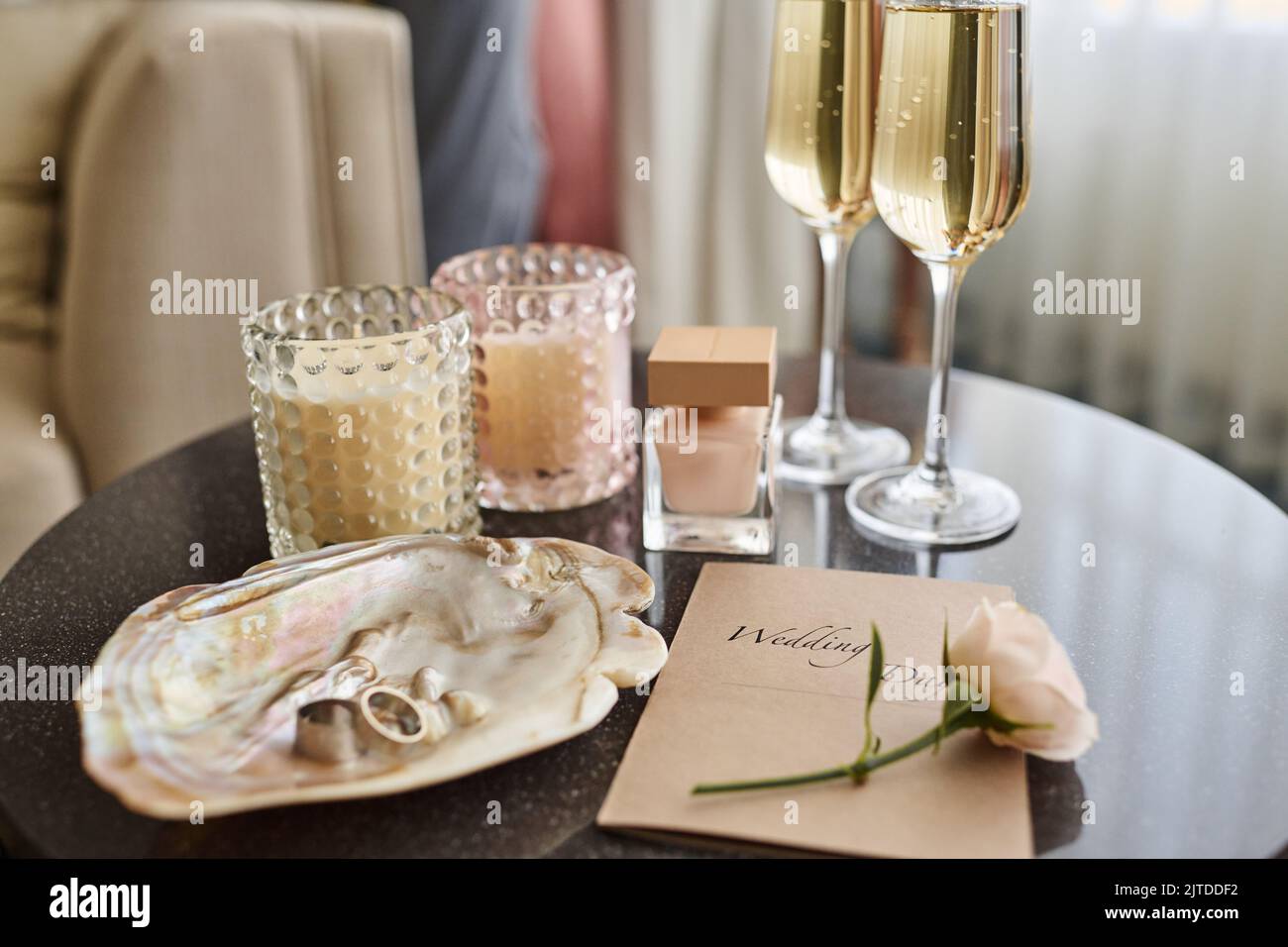 Flauti di champagne, bottiglia di profumo, invito di nozze con rosa bianca e due bicchieri di cocktail creando una composizione romantica Foto Stock