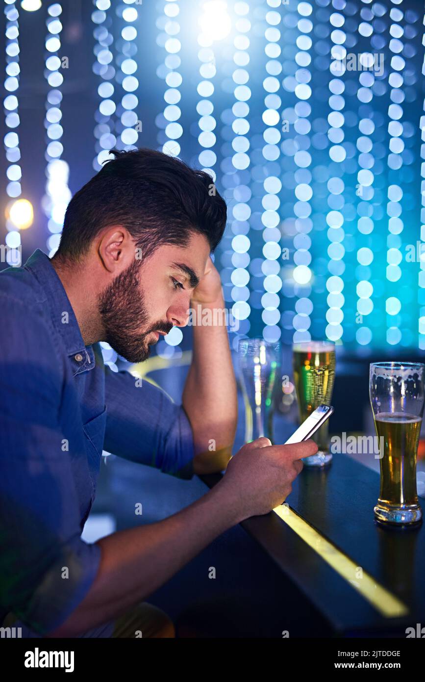 Mescolare alcol e messaggi è un gioco rischioso: Un giovane che guarda turbato mentre usa il telefono al bar. Foto Stock