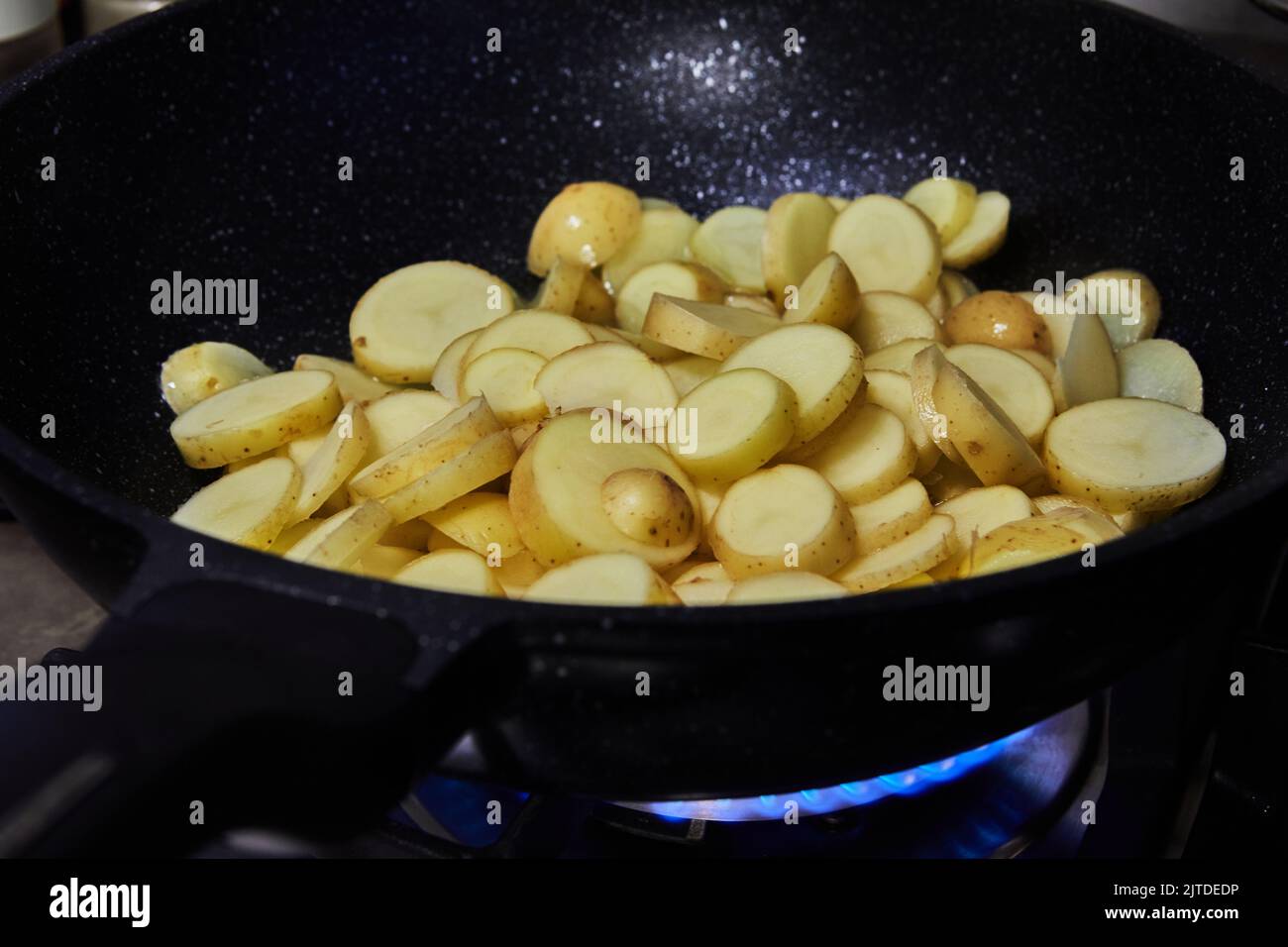 Le patate a fette vengono fritte in padella su stufa a gas Foto Stock