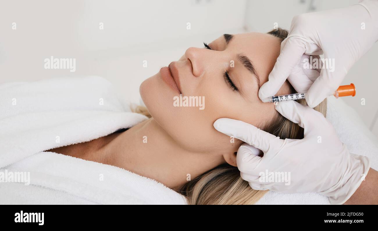 Bella donna durante la mesoterapia facciale per lisciare le rughe mimiche intorno agli occhi con estetista. Iniezioni anti-invecchiamento per ringiovanimento e lift Foto Stock