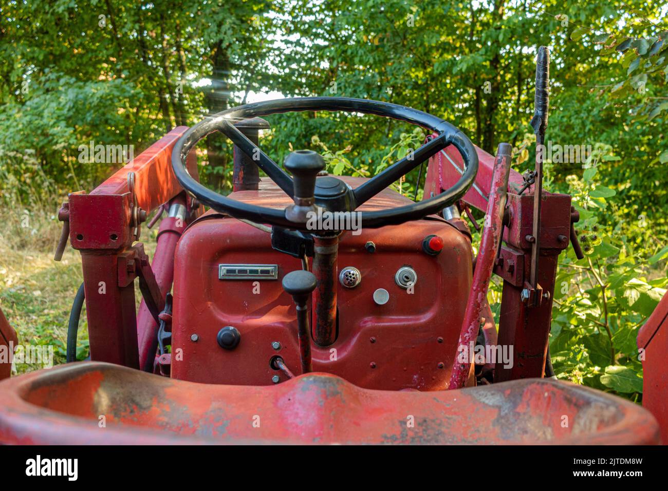 vista dettagliata del sedile del conducente sul volante del vecchio trattore rosso ai margini della foresta Foto Stock