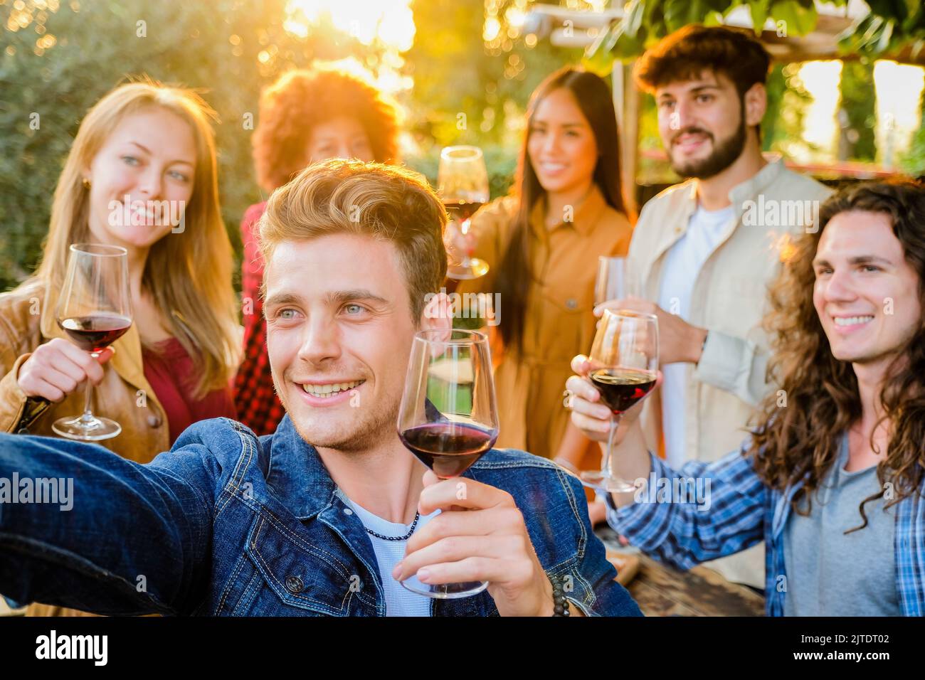 Gruppo di amici multirazziali che prendono selfie e festeggiano con bicchieri da vino a cena in terrazza - giovani che mangiano e bevono vino rosso Foto Stock