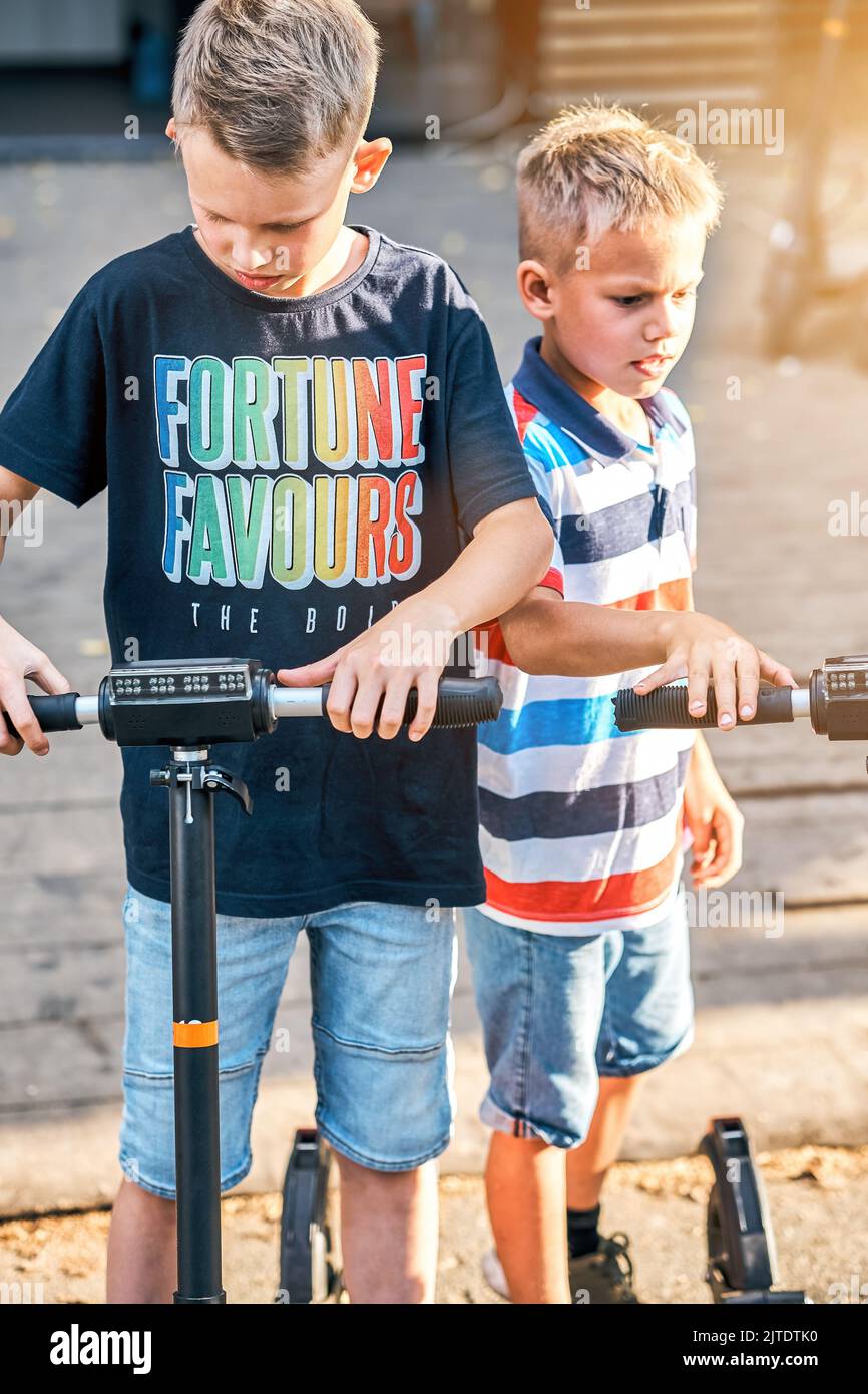 I ragazzi più giovani scelgono lo scooter elettrico presso la stazione di noleggio. Fratelli a piedi nel parco con i genitori. Vacanze attive per tutta la famiglia Foto Stock