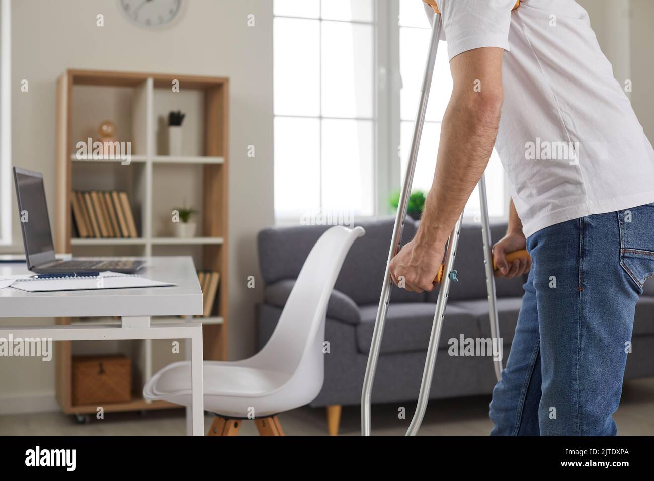 Un giovane che ha disabilità o una gamba ferita rotta cammina sulle stampelle a casa Foto Stock