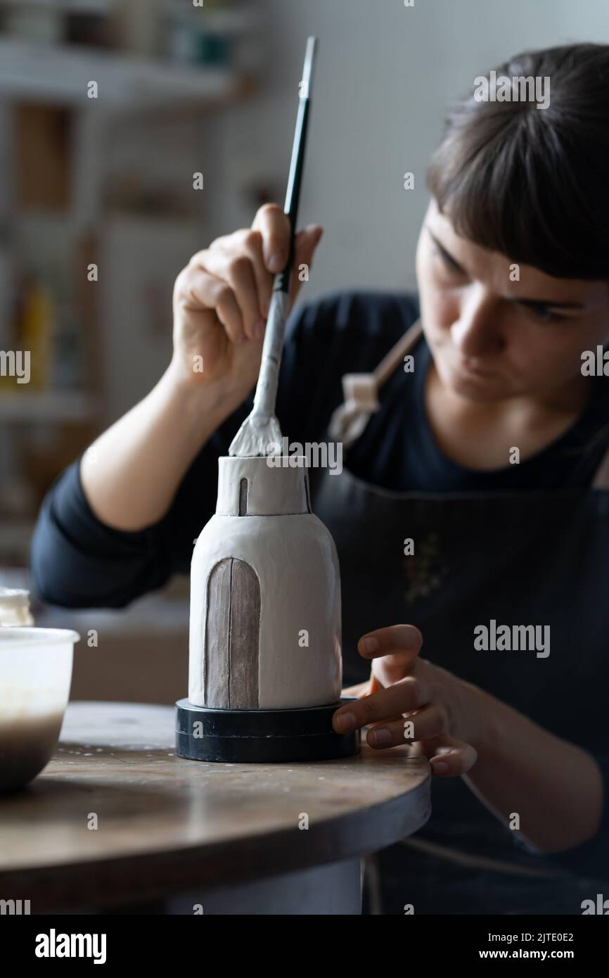 Felice concentrato giovane artigiano dipinge vaso di argilla seduta al tavolo da lavoro primo piano Foto Stock