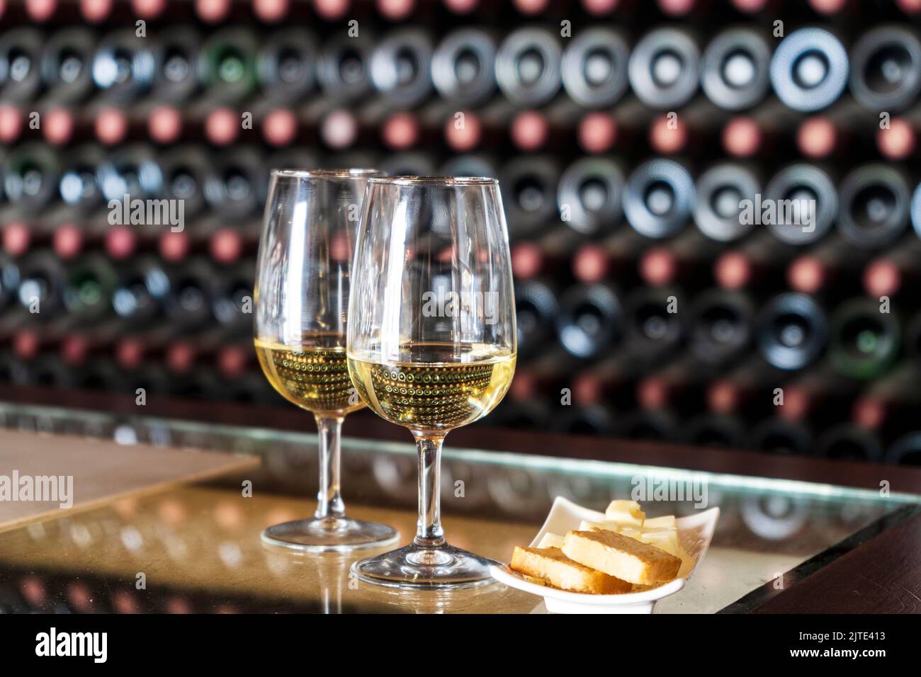 Degustazione di vini in cantina - 2 bicchieri di vino bianco con toast e formaggio con centinaia di bottiglie di vino impilate dietro, Lanzarote, Spagna Foto Stock