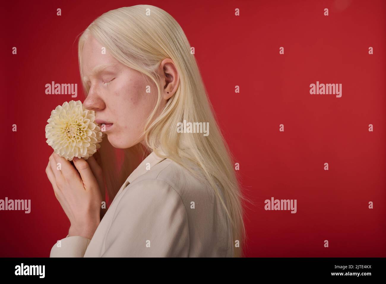 Ritratto di giovane ragazza con aspetto insolito posa con fiore bianco su sfondo rosso Foto Stock