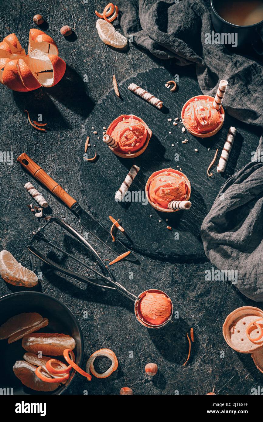 Gelato all'arancia fatto in casa su sfondo scuro con cucchiaio di gelato in acciaio inossidabile, piatto, vista dall'alto Foto Stock