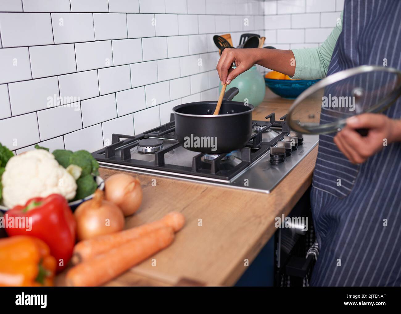 Primo piano di una giovane donna che agita una pentola di cibo su stovetop a gas Foto Stock