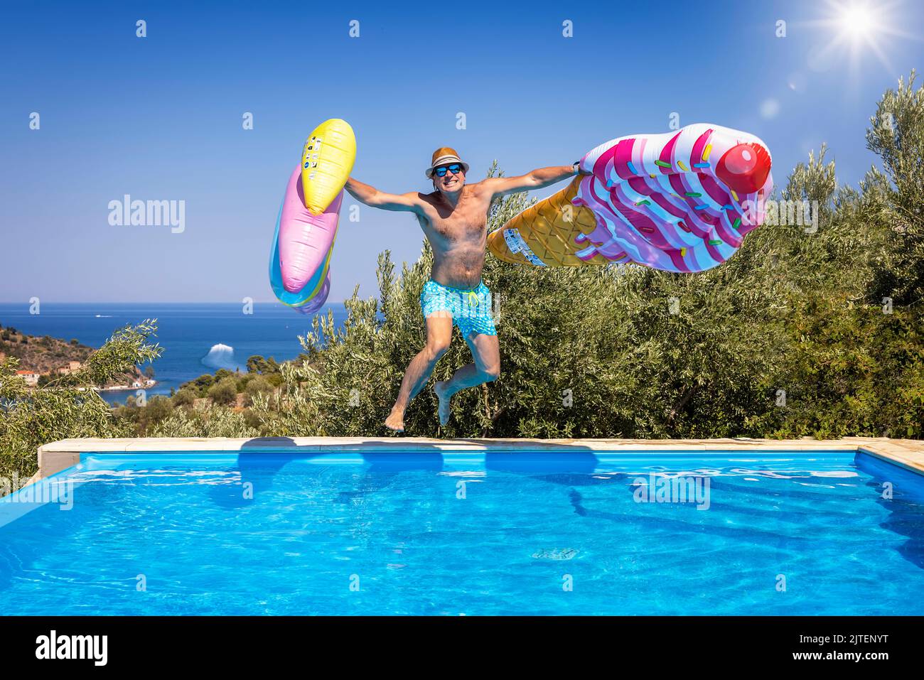 Concetto estivo con un felice uomo di vacanza con cappello e occhiali da sole che saltano in piscina Foto Stock