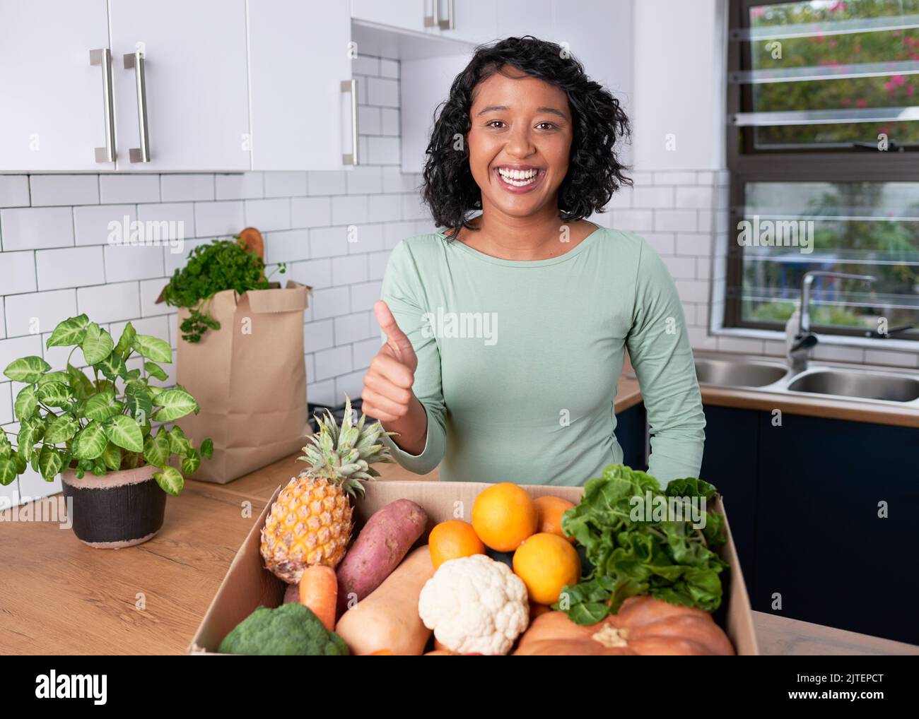 Una giovane donna sorride e dà pollici fino alla consegna di frutta fresca e casella di verdure Foto Stock