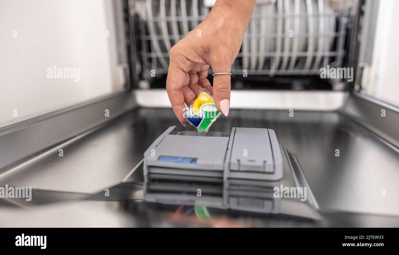 Una compressa per lavastoviglie blu, gialla e verde viene inserita nell'apparecchio con una mano femmina. Foto Stock