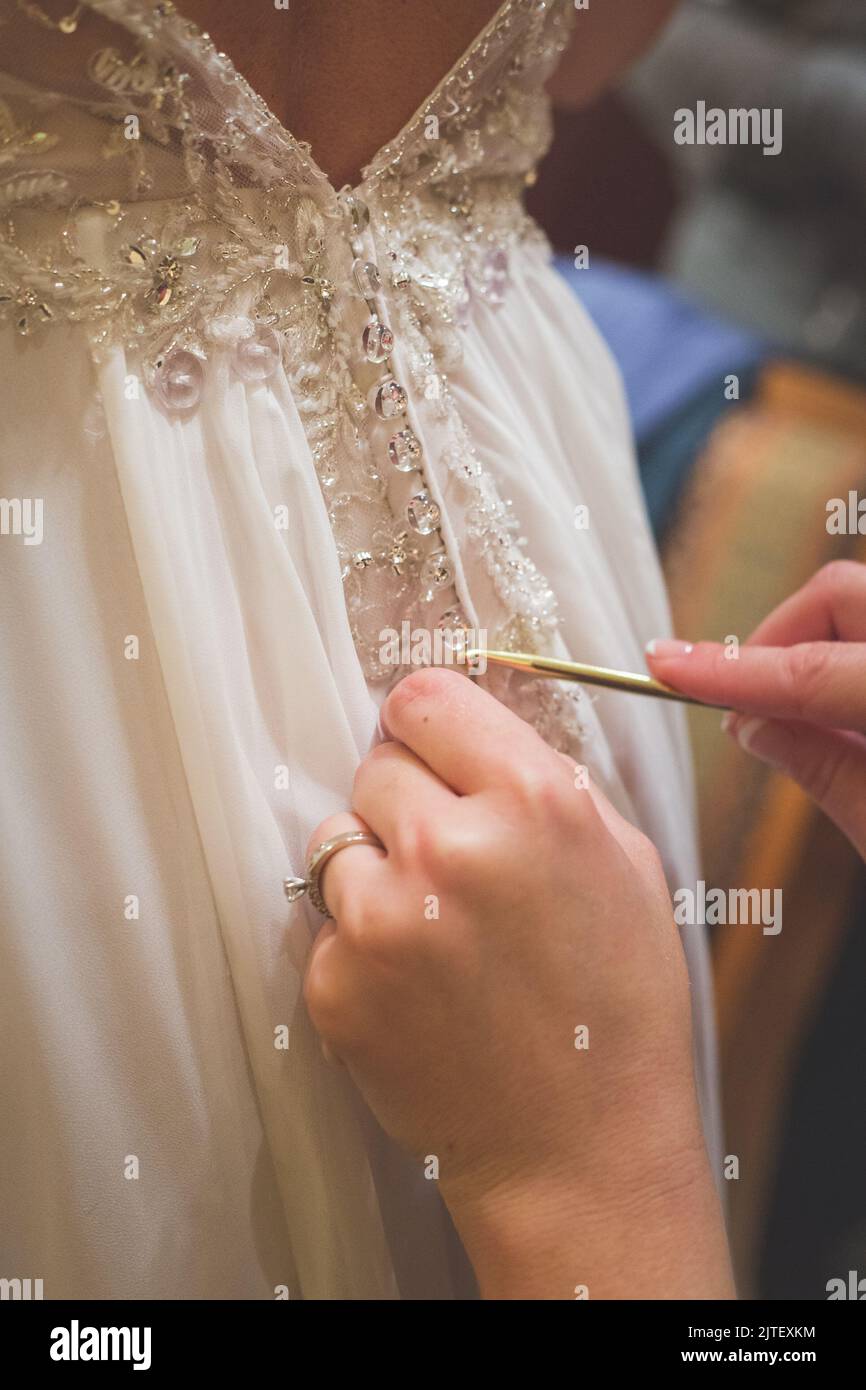 Sposa essere aiutato in vestito di nozze da bridessmaid usando un ago di maglia. Foto Stock