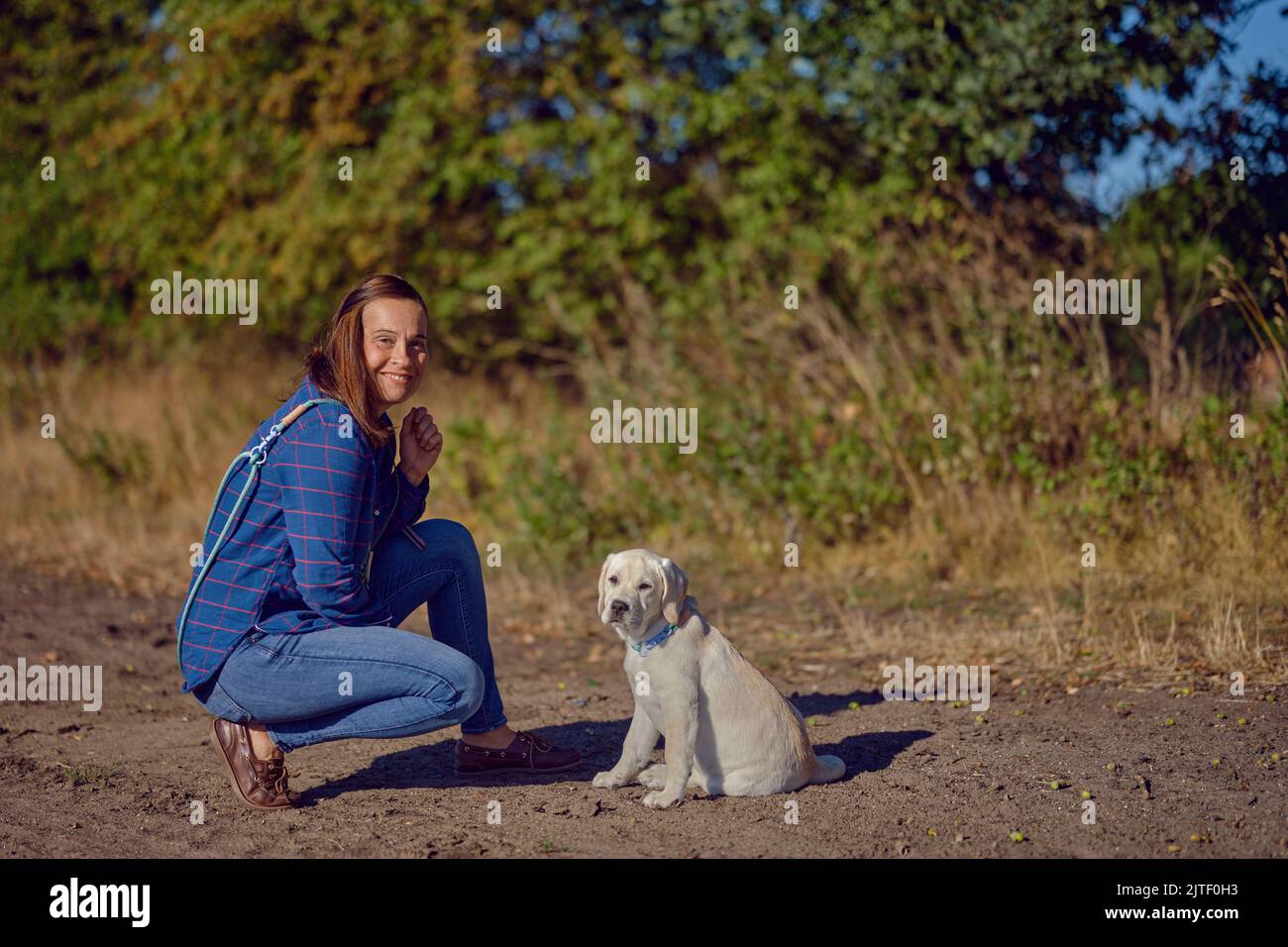 Felice brunetta donna di mezza età che starnutisce con il suo piccolo cucciolo Labrador mentre starnutisce su un sentiero rurale Foto Stock