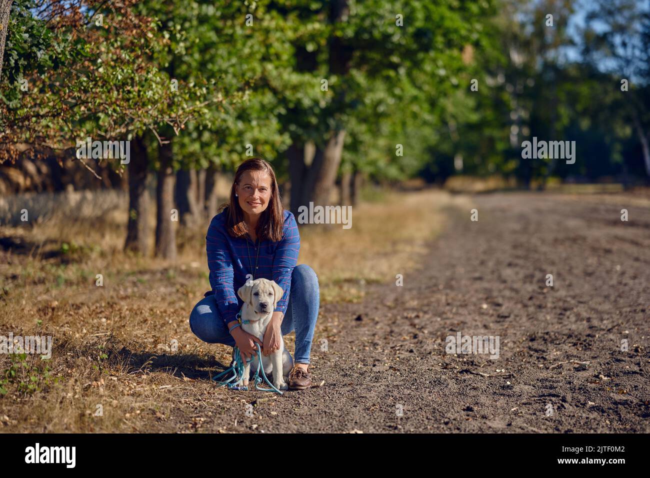 Felice brunetta donna di mezza età che starnutisce con il suo piccolo cucciolo Labrador mentre starnutisce su un sentiero rurale Foto Stock