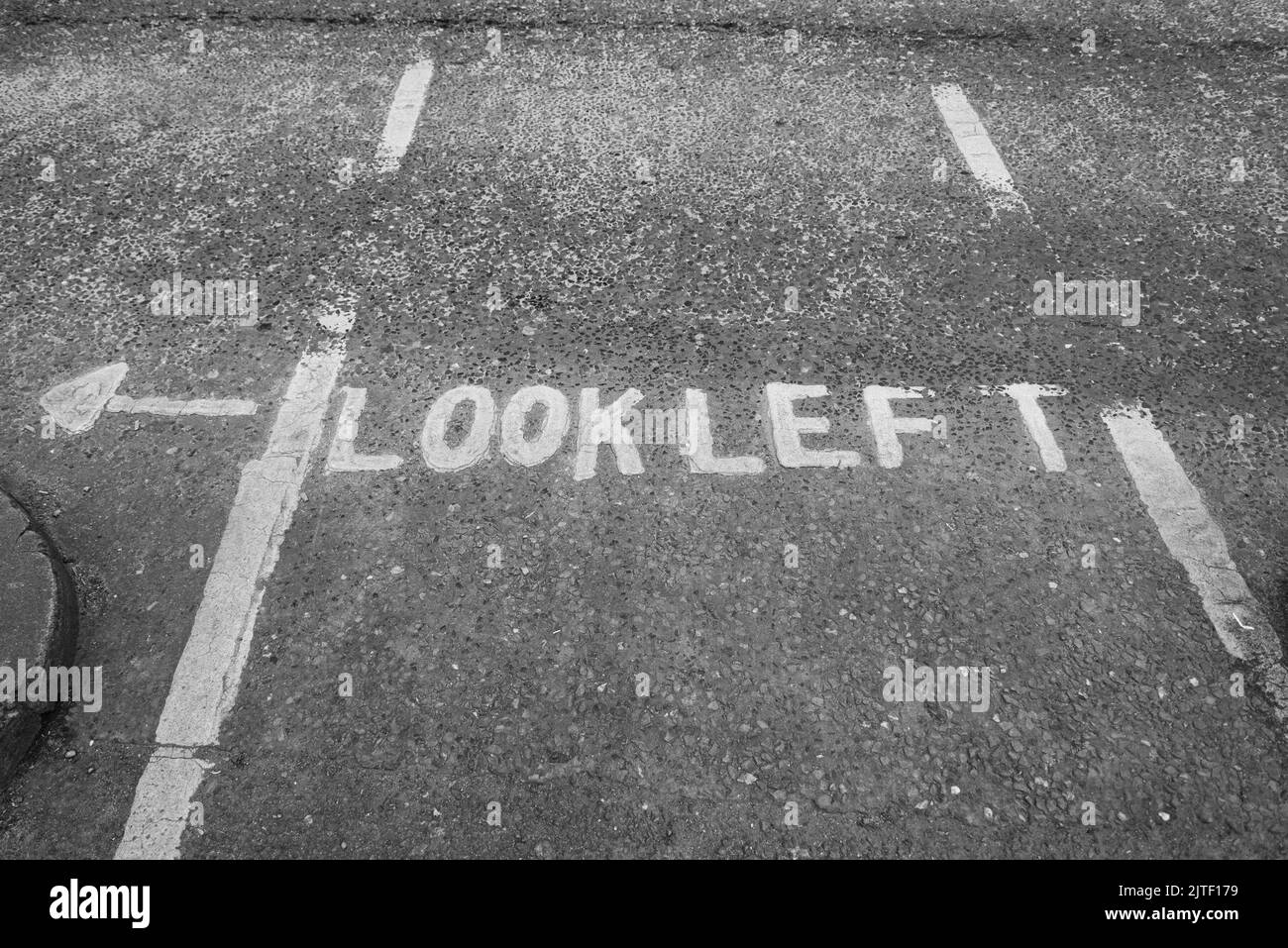 Una strada grigia a Dublino, Irlanda, con un cartello dipinto che dice "Look Left" con una freccia bianca. Foto Stock