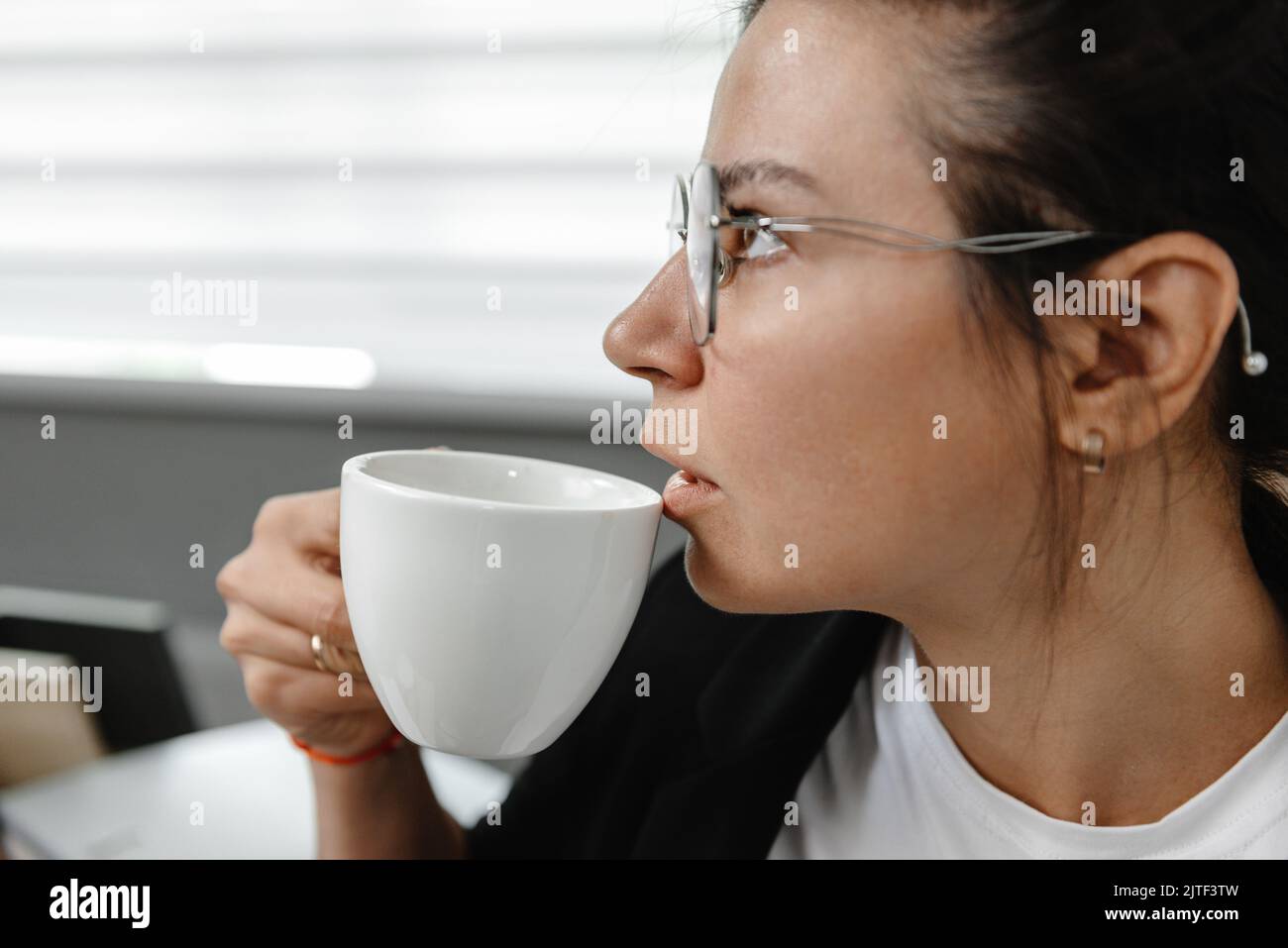 Una ragazza beve caffè in ufficio e pensa. Una ragazza sta pensando, una pausa nel suo lavoro. Il dipendente in ufficio non sorride e beve caffè Foto Stock