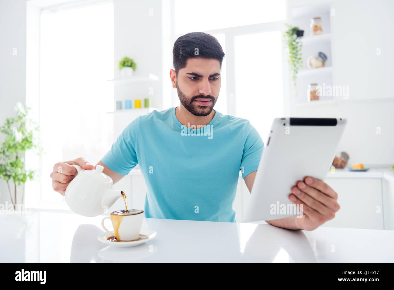 Foto della persona concentrata concentrata tenere utilizzare tablet versare caffè versato su una tazza di cucina al coperto Foto Stock