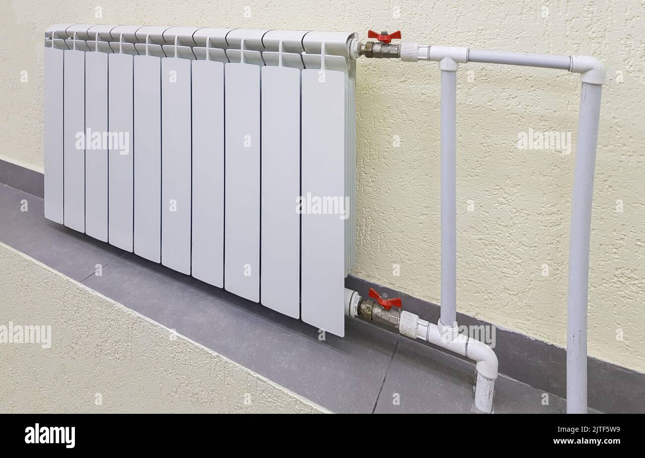 Moderna batteria bianca in alluminio per il riscaldamento dell'acqua calda, sullo sfondo di una parete all'interno di un appartamento o di uno spazio ufficio. Foto Stock