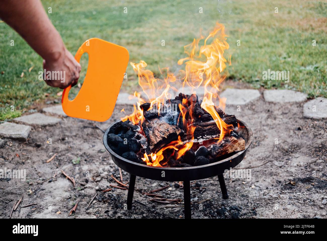 Come usare una griglia di carbone. Uomo con ventilatore a mano barbecue di plastica vicino al fuoco del grill di carbone. Barbecue in plastica BBQ ventilatore a mano Foto Stock