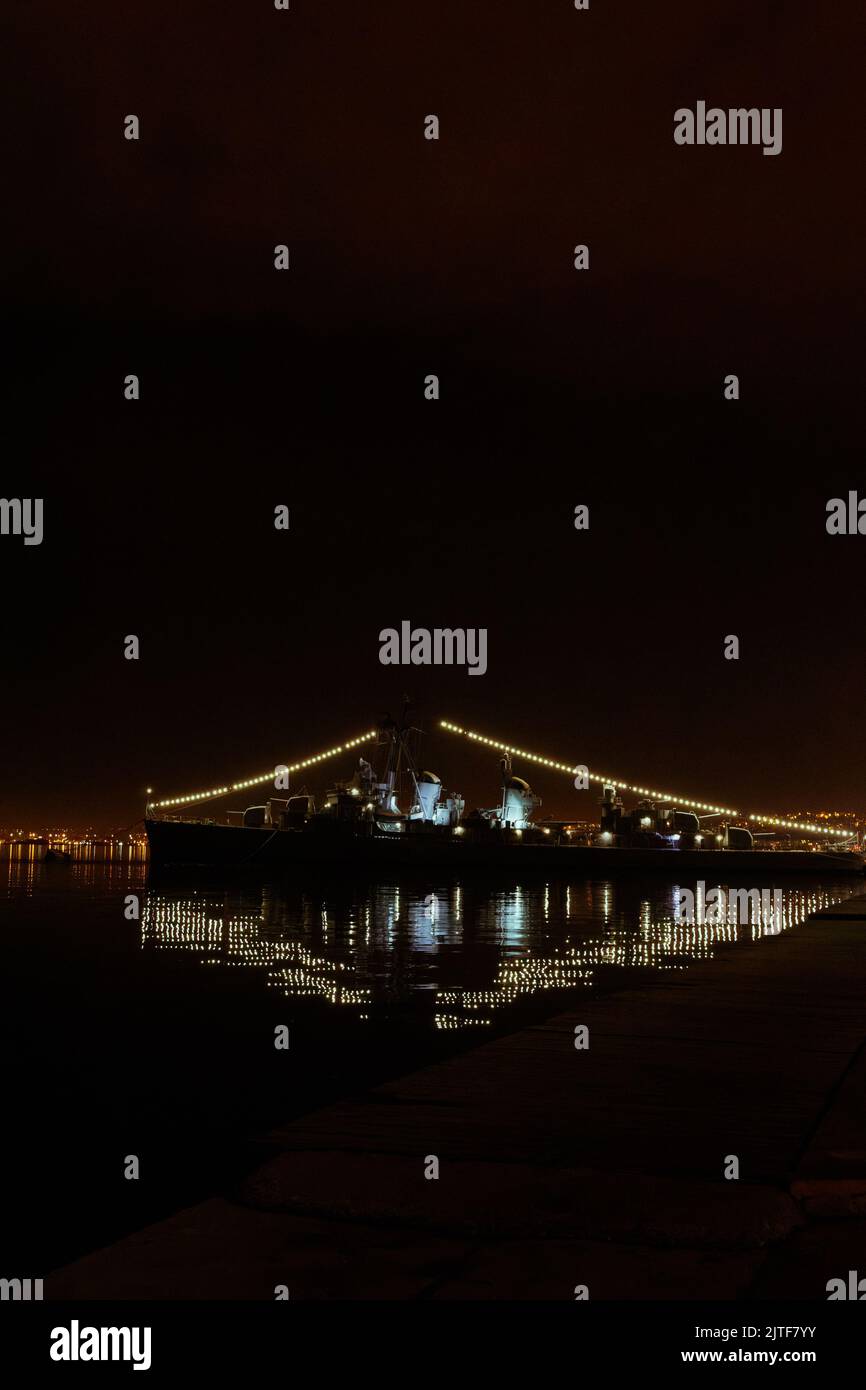 Vista notturna della storica nave da guerra greca illuminata del WW2 ormeggiata contro il cielo scuro. Foto Stock