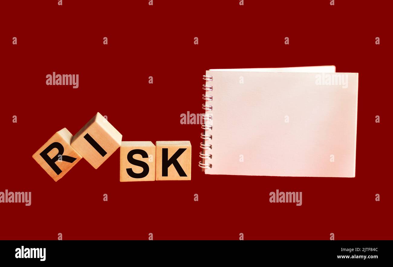 Cubi di legno con la parola rischio su sfondo rosso con un blocco note. Concetto di accettazione, gestione o valutazione dei rischi. Eliminare i rischi durante il makein Foto Stock
