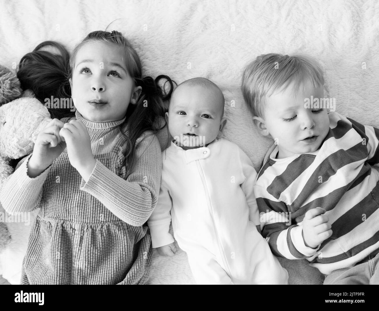 Fratello e sorella (2-3) con neonato (0-1 mesi) a letto Foto Stock