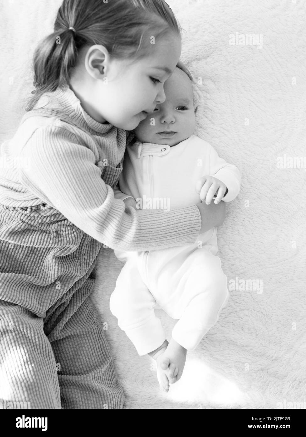 Ragazza (2-3) che abbraccia il fratello neonato (0-1 mesi) a letto Foto Stock