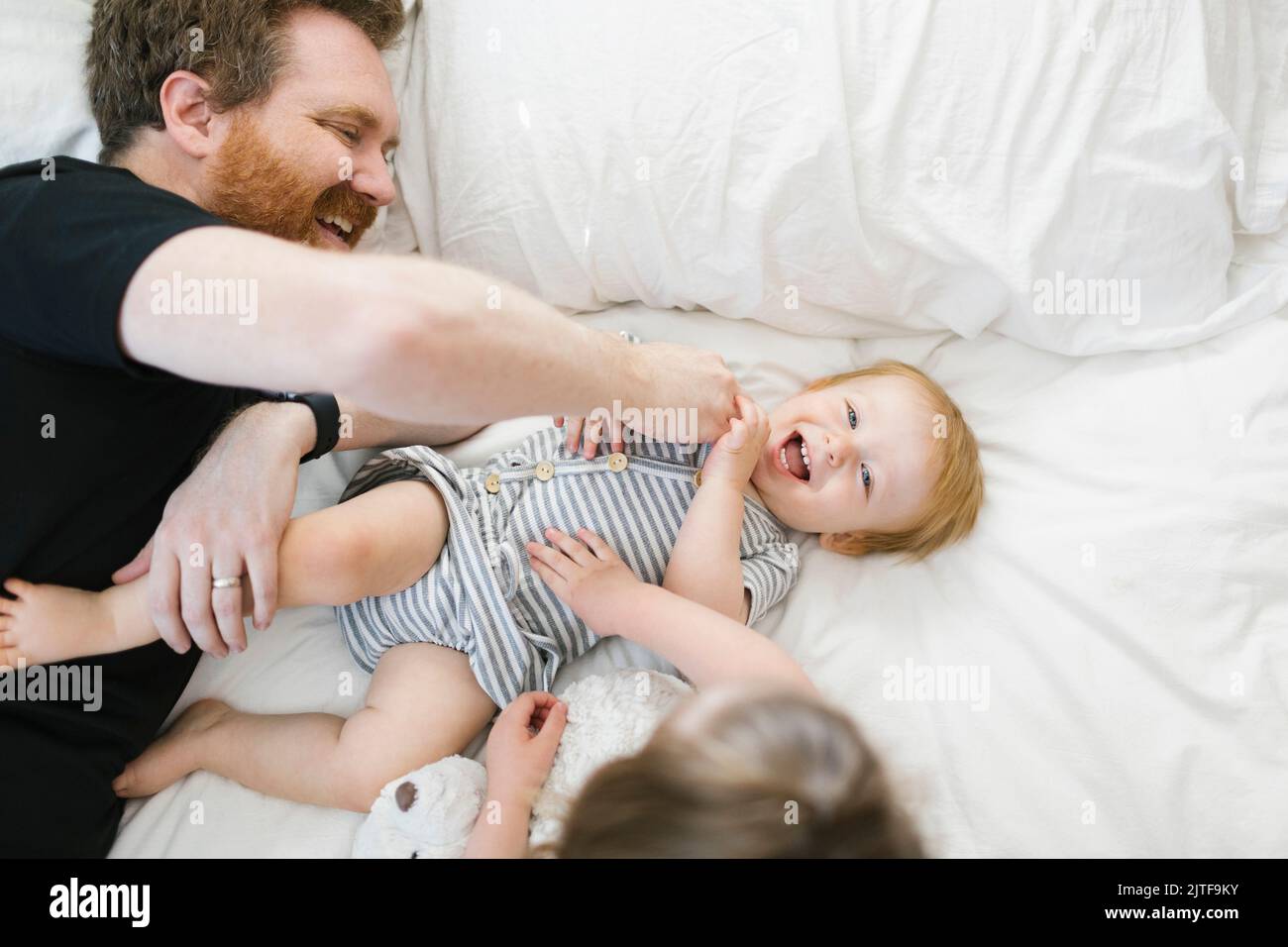 Padre che gioca con il figlio (12-17 mesi) e la figlia (2-3) a letto Foto Stock