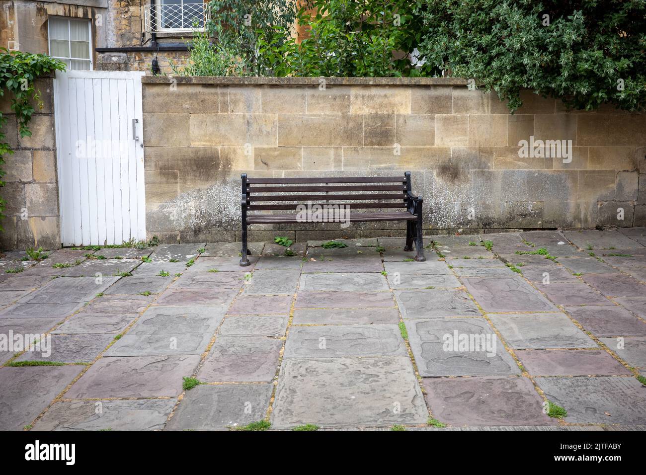 Panca vuota in legno accanto ad un muro di pietra a Bath, UK (Aug22) Foto Stock